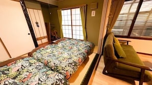 Ein Zimmer mit zwei Betten, einem grünen Sofa, einem Fenster mit Vorhängen und einer Schiebetür.