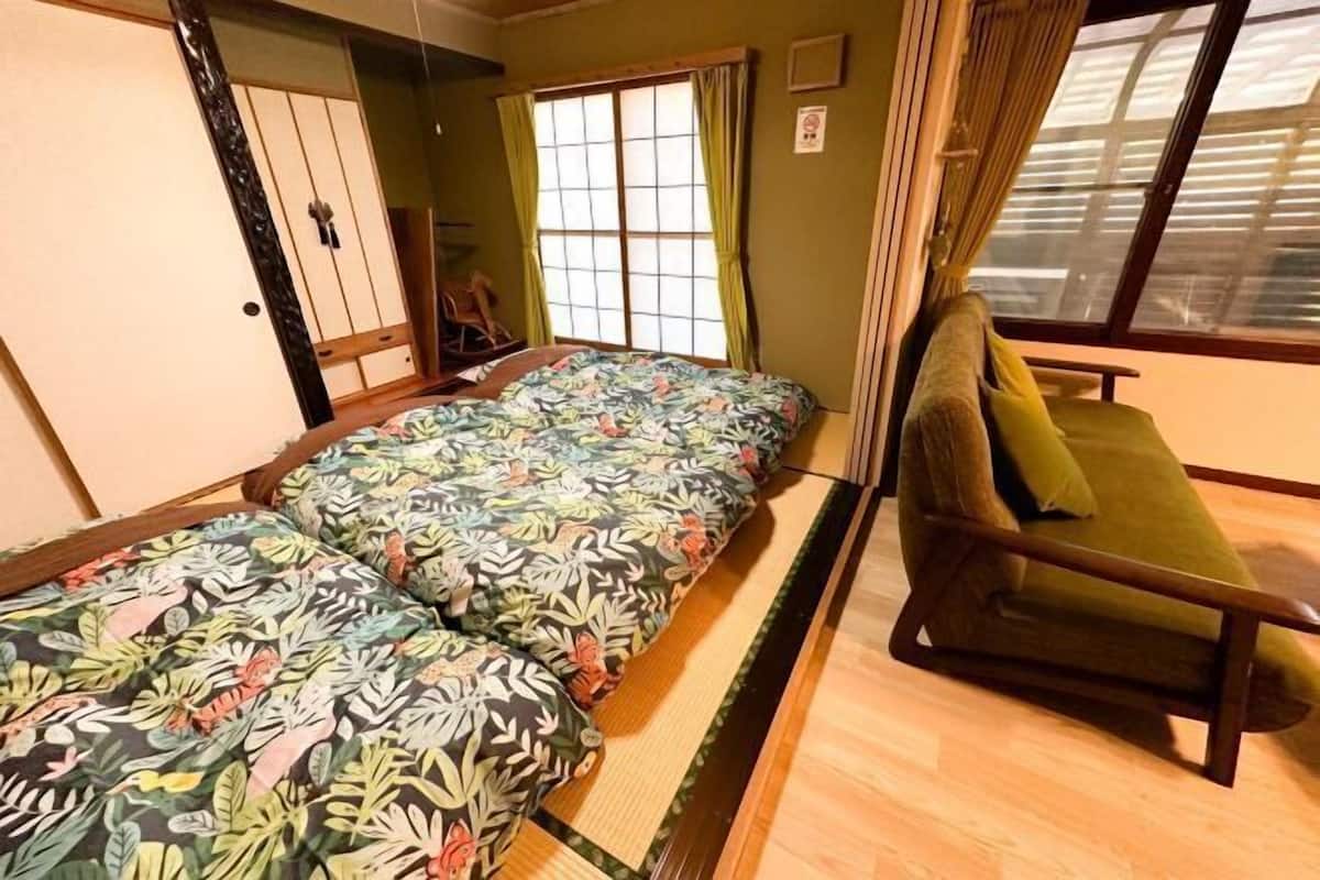 Una habitación con dos camas, un sofá verde, una ventana con cortinas y una puerta corrediza.
