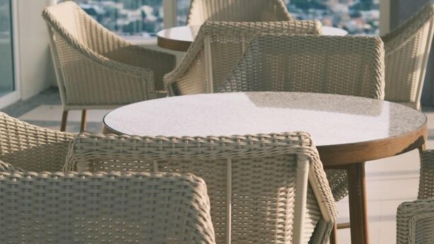 Una mesa redonda con sillas de mimbre en una habitación con ventanas amplias.