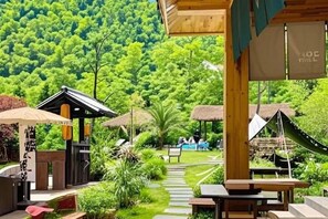 A resort with outdoor seating areas, a thatched-roof structure, and a view of a lush green forest. - TreehouseRiddle (Pasig)