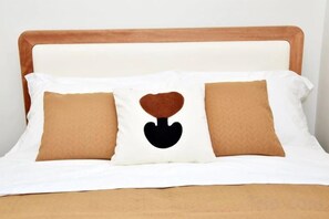 A bed with a white headboard, two brown pillows, and a central pillow with a black heart design. - TreehouseRiddle (Pasig)
