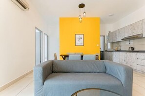 A modern living room with a sofa, a dining table, and a kitchen in the background.