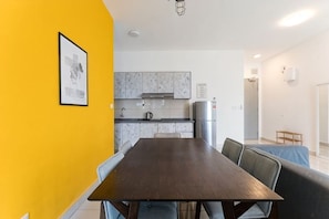 A dining area with a long table and chairs, a kitchen with white cabinets, and a yellow wall. - TR Residence BY FEEL HOME (Kuala Lumpur)