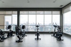 A gym with exercise equipment and large windows overlooking a cityscape. - TR Residence BY FEEL HOME (Kuala Lumpur)