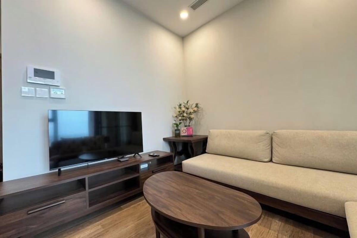 A modern living room with a flat-screen TV, a sofa, a coffee table, and a small side table with a plant.