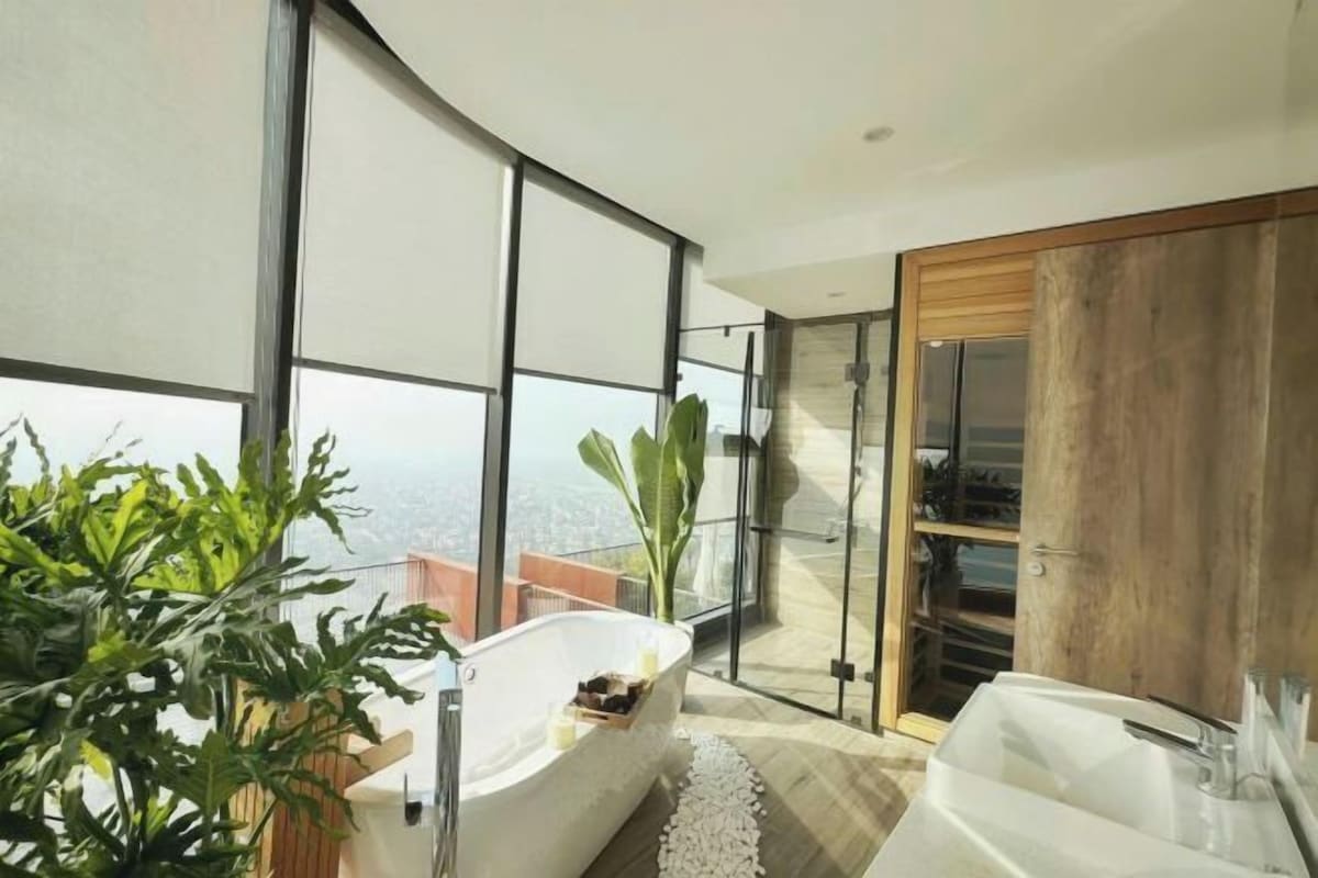 A modern bathroom with a freestanding bathtub, a large mirror, and a view of the city.