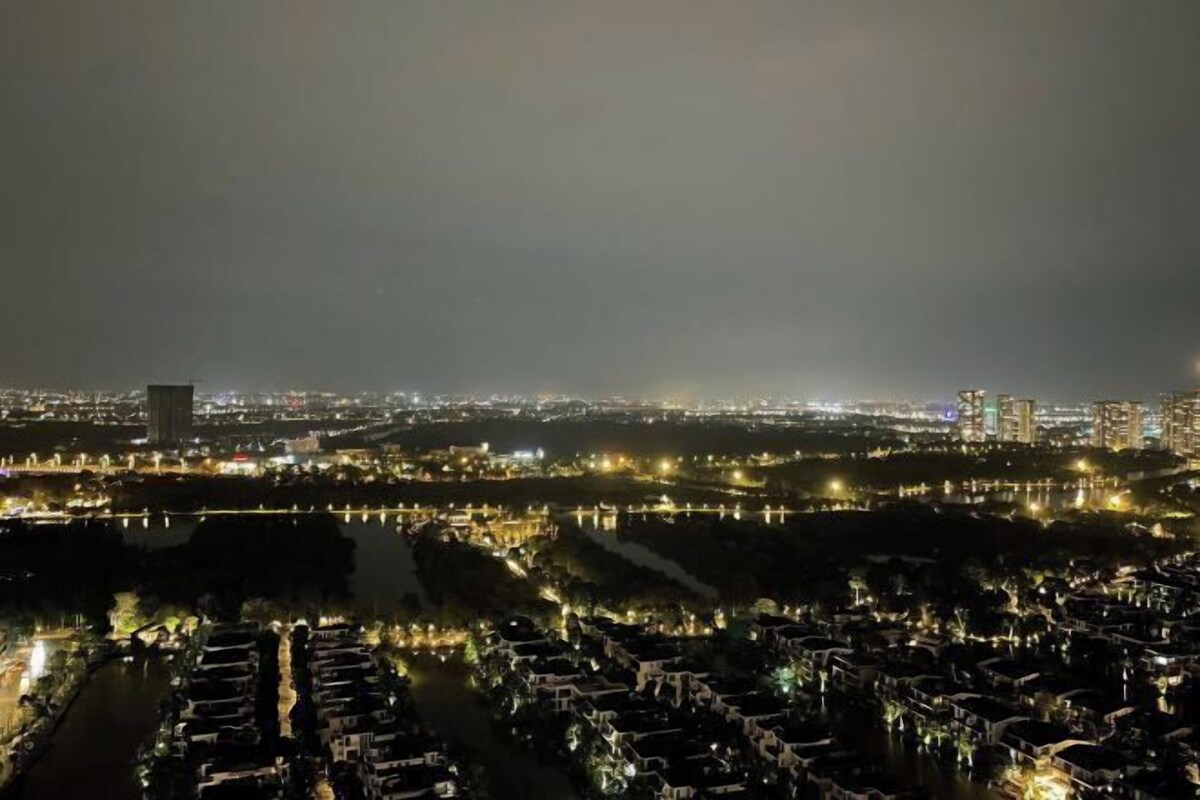 A nighttime cityscape with illuminated buildings, a river, and a bridge.