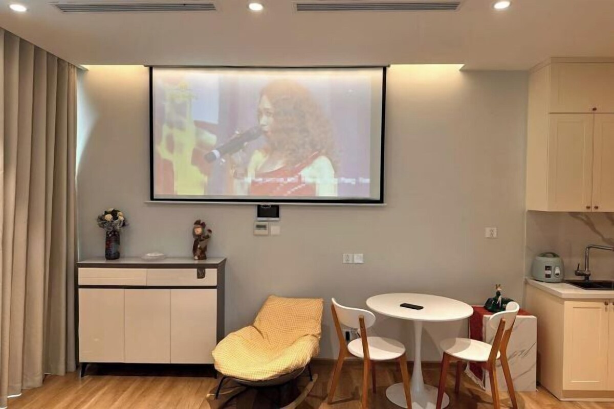 A room with a projector screen, a dining table, chairs, a sofa, a kitchen area, and a cabinet.