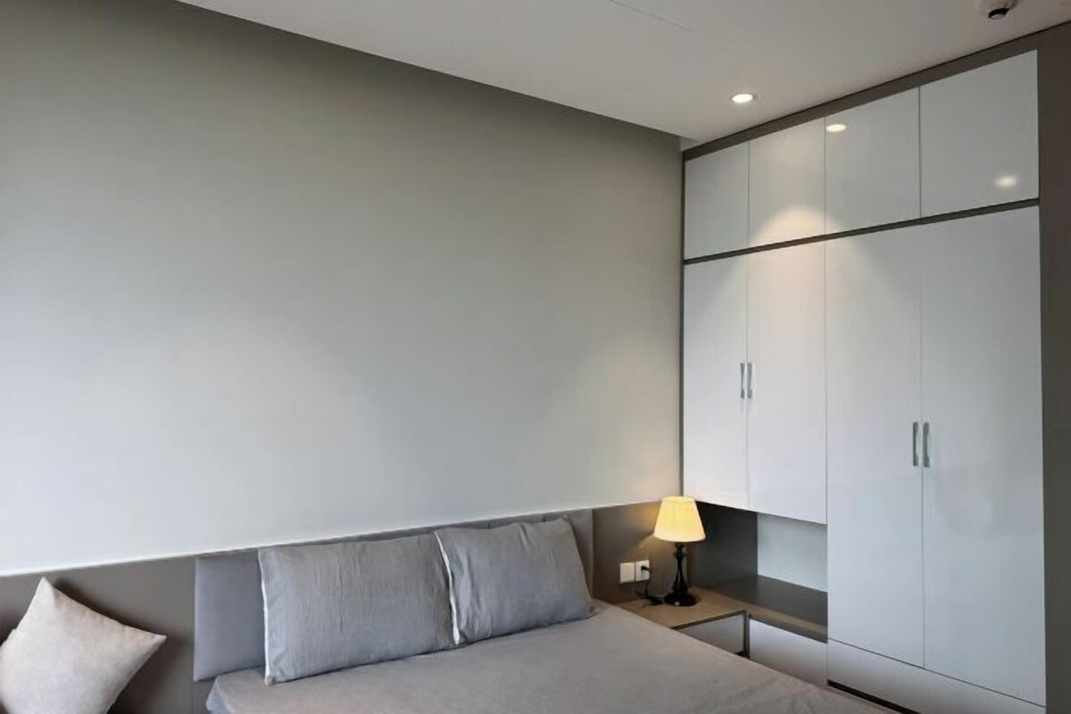 A modern hotel room with a bed, a nightstand, a lamp, and built-in wardrobes.