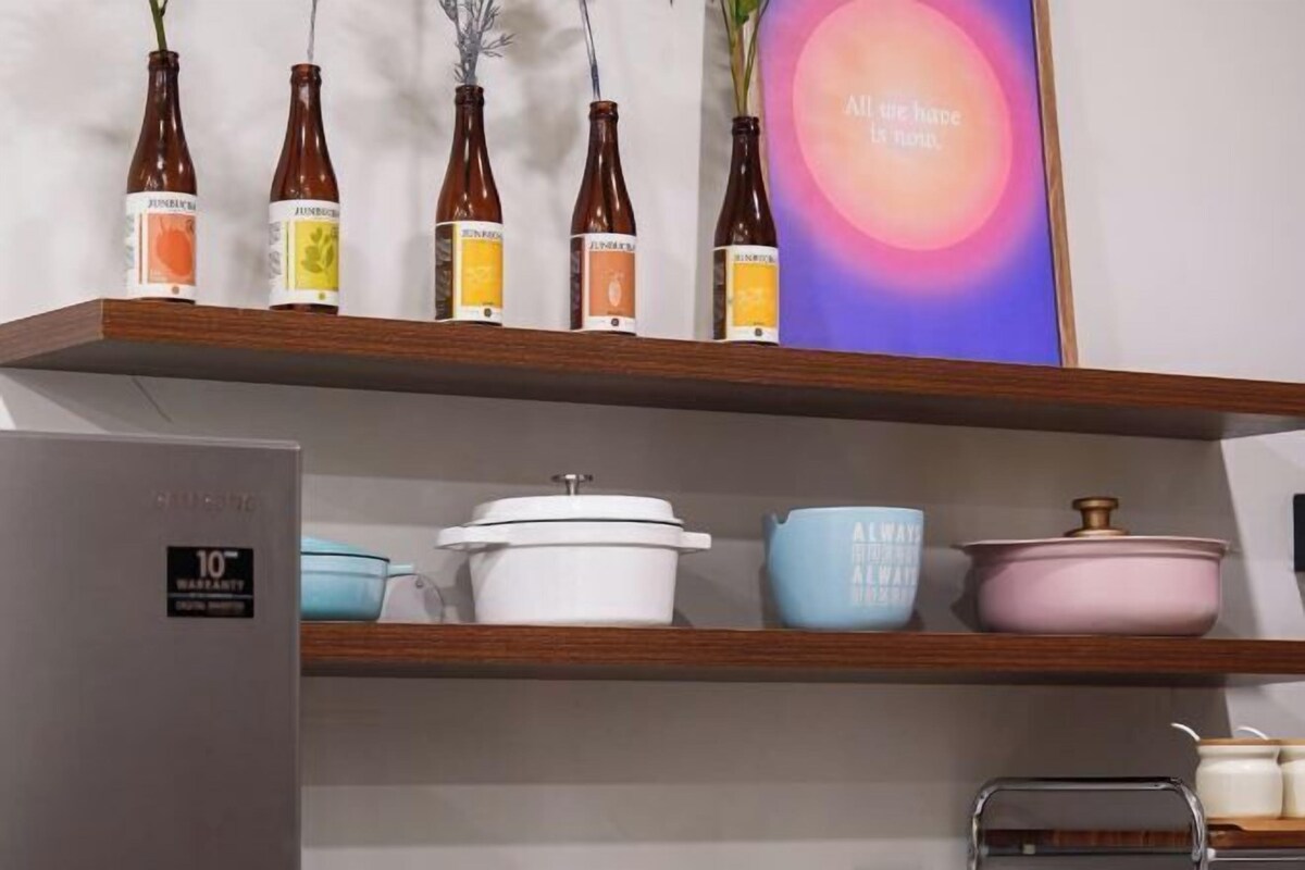 A kitchen shelf with bottles, a white pot, and a pink pot.