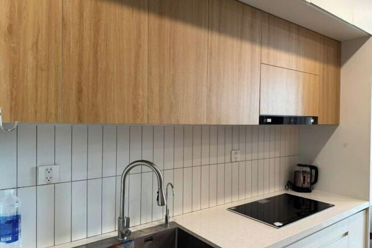 Une cuisine avec des meubles de rangement en bois, un évier en acier inoxydable et une plaque de cuisson à induction noire.