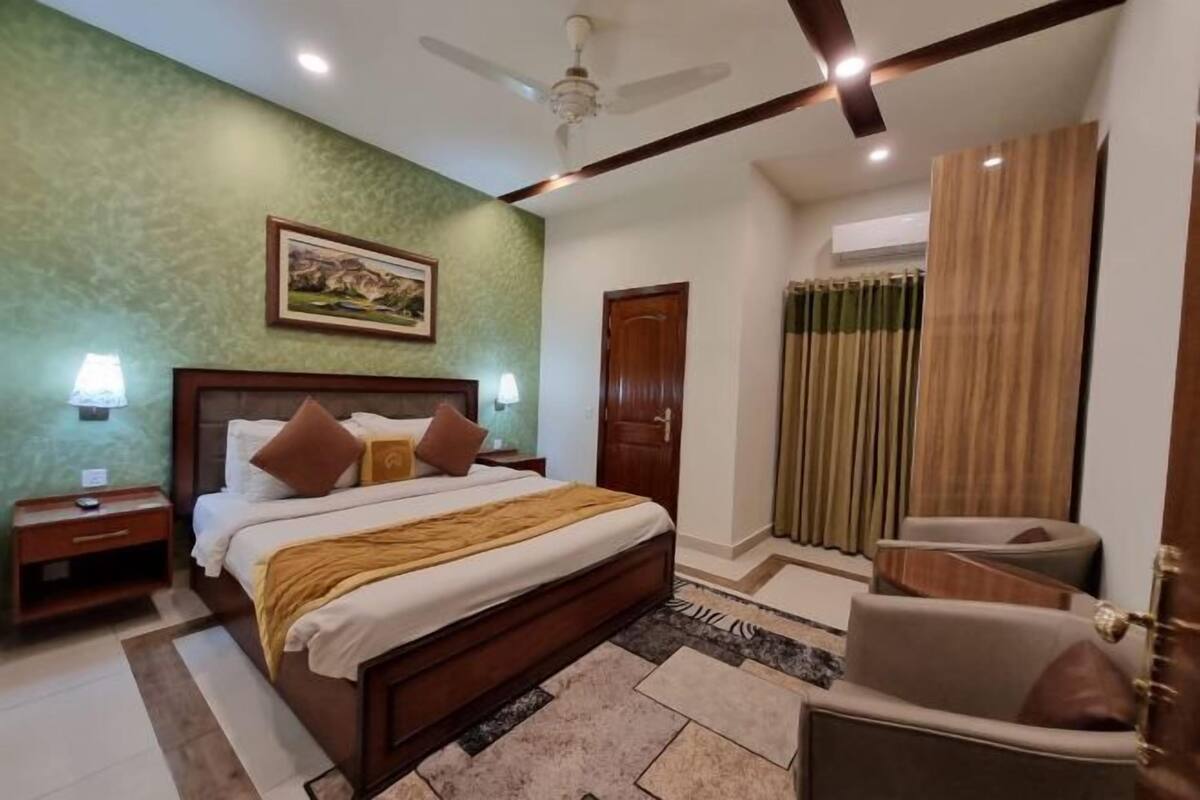 A bedroom with a bed, bedside tables, a chair, a ceiling fan, a door, and a window with curtains.