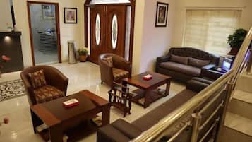 A spacious living area with a sofa, armchairs, and a coffee table. A staircase with a metal railing is visible in the background.