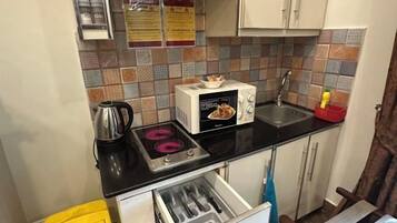 Una cocina compacta con estufa a gas, microondas, pileta y un mueble pequeño.