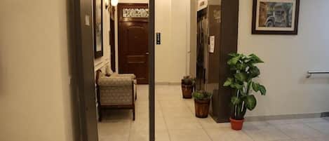 A hotel hallway with a reception desk, a door, and a potted plant.