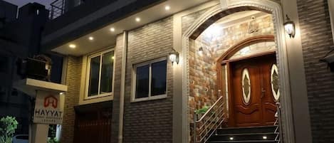 Un edificio con fachada de piedra, puerta principal de madera y una escalera, y un cartel que dice 'HAYYAT'.