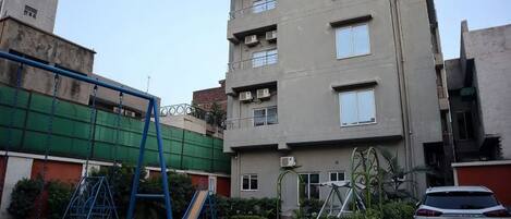 A residential building with a playground, a car parked in front, and a clear sky.