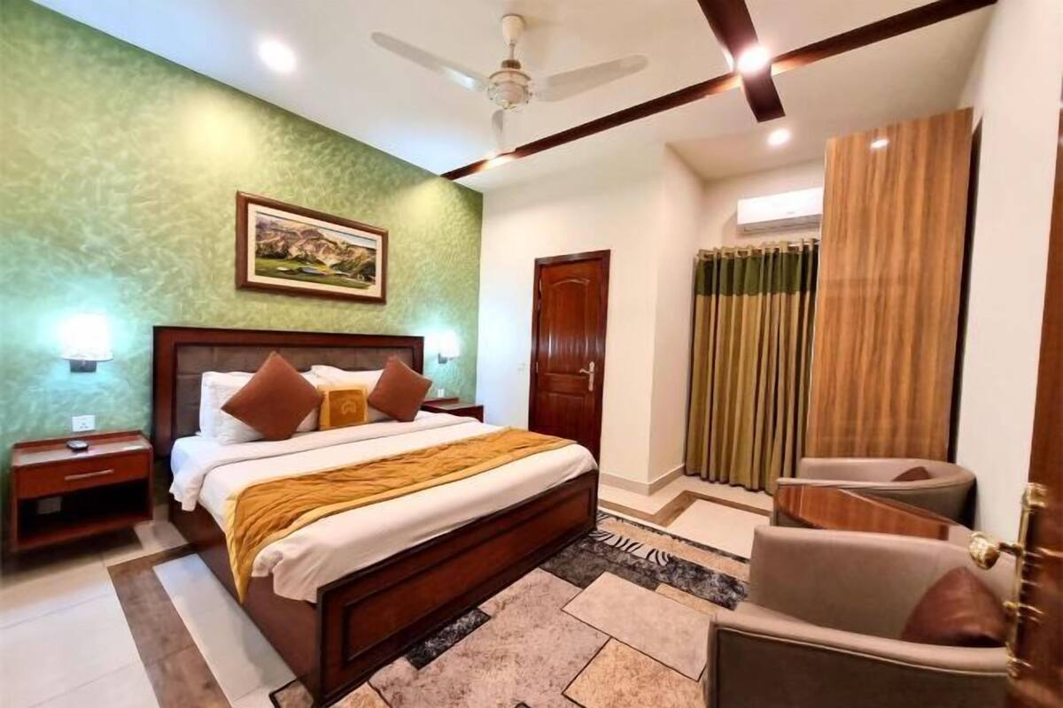 A bedroom with a bed, nightstands, a chair, a ceiling fan, a door, and curtains.