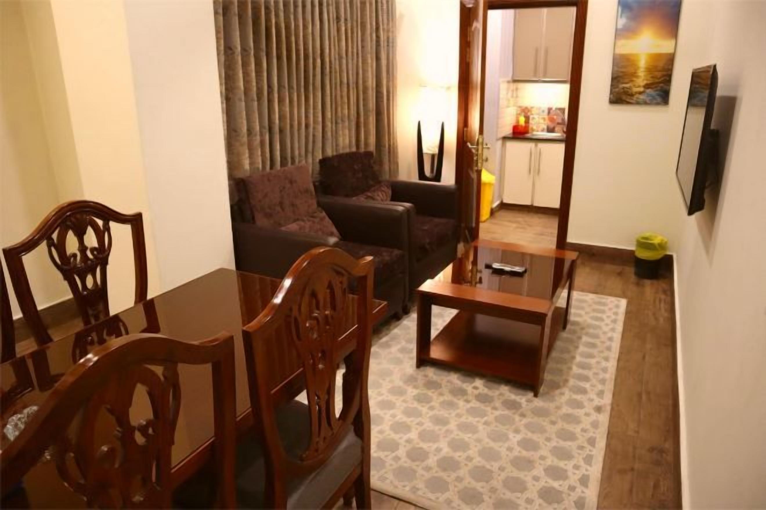 Una sala de estar con un sofá, una mesa de comedor y sillas. Se ve una cocina al fondo.