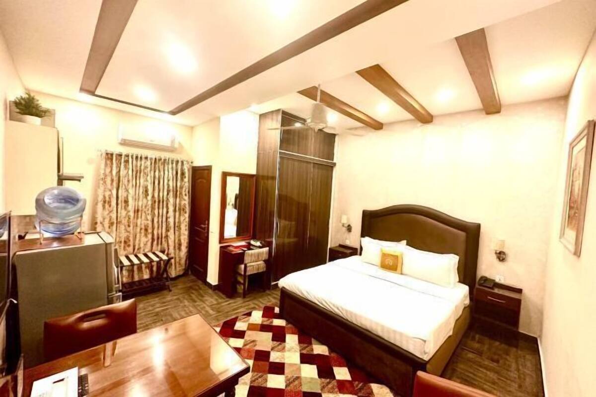 A hotel room with a bed, a desk, a chair, a wardrobe, and a large mirror.