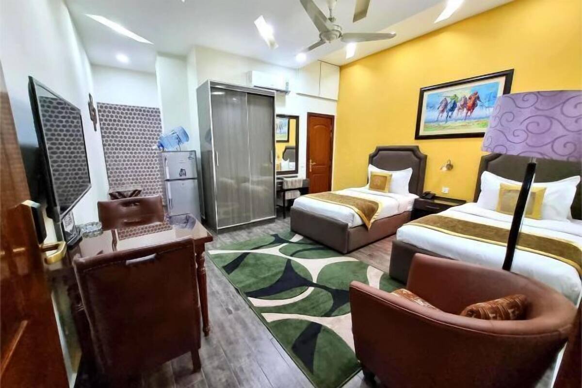 A hotel room with a bed, a desk, a chair, a wardrobe, a mirror, and a painting on the wall.