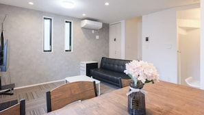 A modern living room with a wooden dining table, a black leather sofa, and a vase of flowers. - Four Seasons Yado 1 (Tokyo)