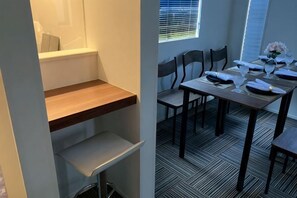 A dining area with a table set for two, chairs, a window with blinds, and a patterned floor. - Four Seasons Yado 1 (Tokyo)