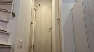 A narrow hallway with a wooden door at the end, a light switch on the wall, and a door handle.