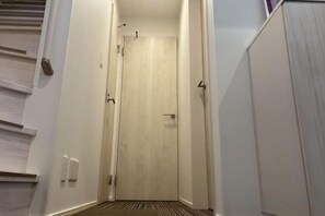 A narrow hallway with a wooden door at the end, a light switch on the wall, and a door handle. - Four Seasons Yado 1 (Tokyo)