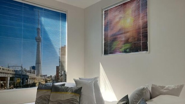 A hotel room with a bed, pillows, a window with a cityscape view, and blinds. - Four Seasons Yado 1 (Tokyo)