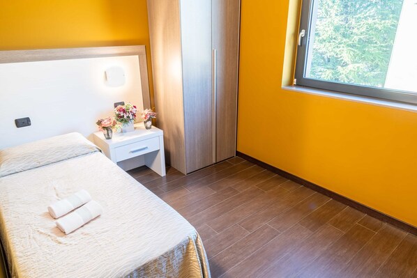 A hotel room with a bed, a nightstand, a window with a view of trees, and a wooden floor. - hotel ferrari milano (Carugate)