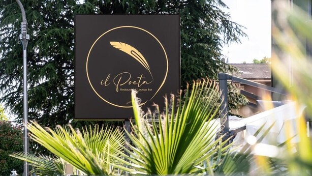 A sign for 'Il Poeta Restaurant & Lounge Bar' with a feather logo, surrounded by palm plants and a street view. - hotel ferrari milano (Carugate)