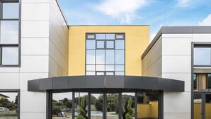 A modern building with a curved entrance, large windows, and a yellow facade. - hotel ferrari milano (Carugate)