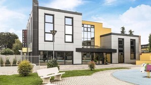 A modern hotel with a flat roof, large windows, and a paved outdoor area with benches and a small play area. - hotel ferrari milano (Carugate)