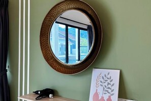 A round mirror with a textured frame on a wall, a small table with a phone, and a framed picture of vases with leaves. - Sunway Ipoh - DamaiStay - 5Min to Tambun - 20Pax (Kinta)