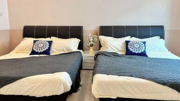 Zwei Einzelbetten mit schwarzen Kopfteilen und weißer Bettwäsche, ein kleiner Nachttisch mit Blumenvase und eine schlichte Wand im Hintergrund.