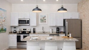 A modern kitchen with white cabinets, stainless steel appliances, a granite countertop, and two pendant lights.