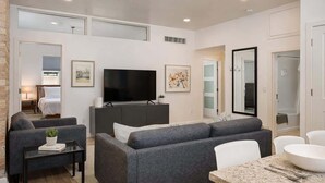 A modern living room with a flat-screen TV, grey sofas, a coffee table, and a dining area with a granite table.