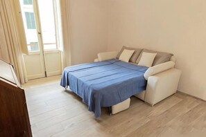 Un dormitorio con cama, sofá, piso de madera y una ventana.