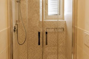 Eine Duschkabine mit Handbrause, einem Handtuchhalter und einem Fenster mit Jalousien.