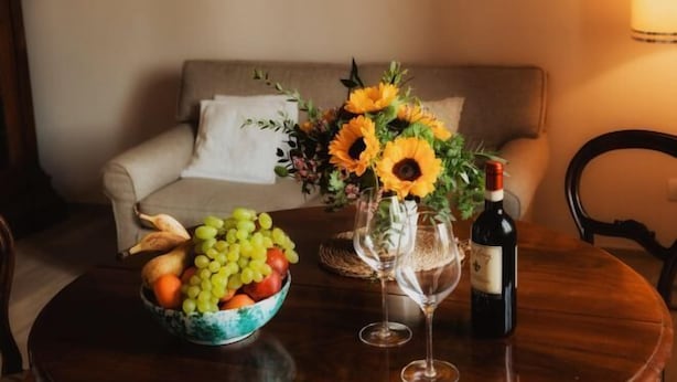 A round wooden table with a bowl of fruit, a vase with sunflowers, a wine bottle, and a wine glass. - Modern apartments in the heart of Florence (Florence)