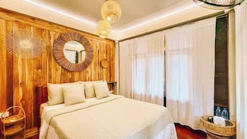 Un dormitorio con una cama grande, paredes de paneles de madera, un espejo redondo y una mesita de mimbre.