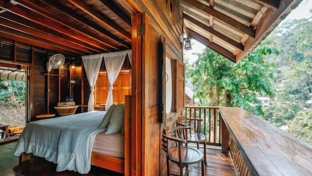 Una stanza in legno con un letto, una ventola e un balcone affacciato sul verde.