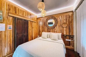 A bedroom with a wooden wall paneling, a bed with white bedding, a round mirror, and a hanging light fixture. - Himdoihome Maekampong (Mae On)