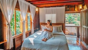 Una baita di legno con un letto, tende e vista sul verde.