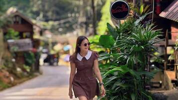 Una persona caminando por una carretera con follaje y edificios al fondo.
