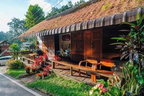 A traditional wooden building with a sloped roof, outdoor seating, and a garden area with flowers. - Himdoihome Maekampong (Mae On)