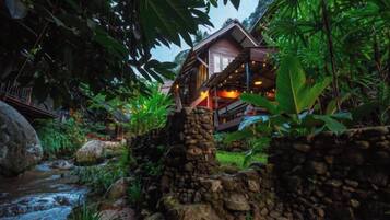 A rustic stone structure with a wooden deck and a house in the background.