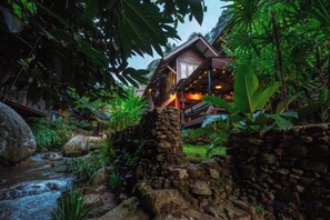 A rustic stone structure with a wooden deck and a house in the background. - Himdoihome Maekampong (Mae On)
