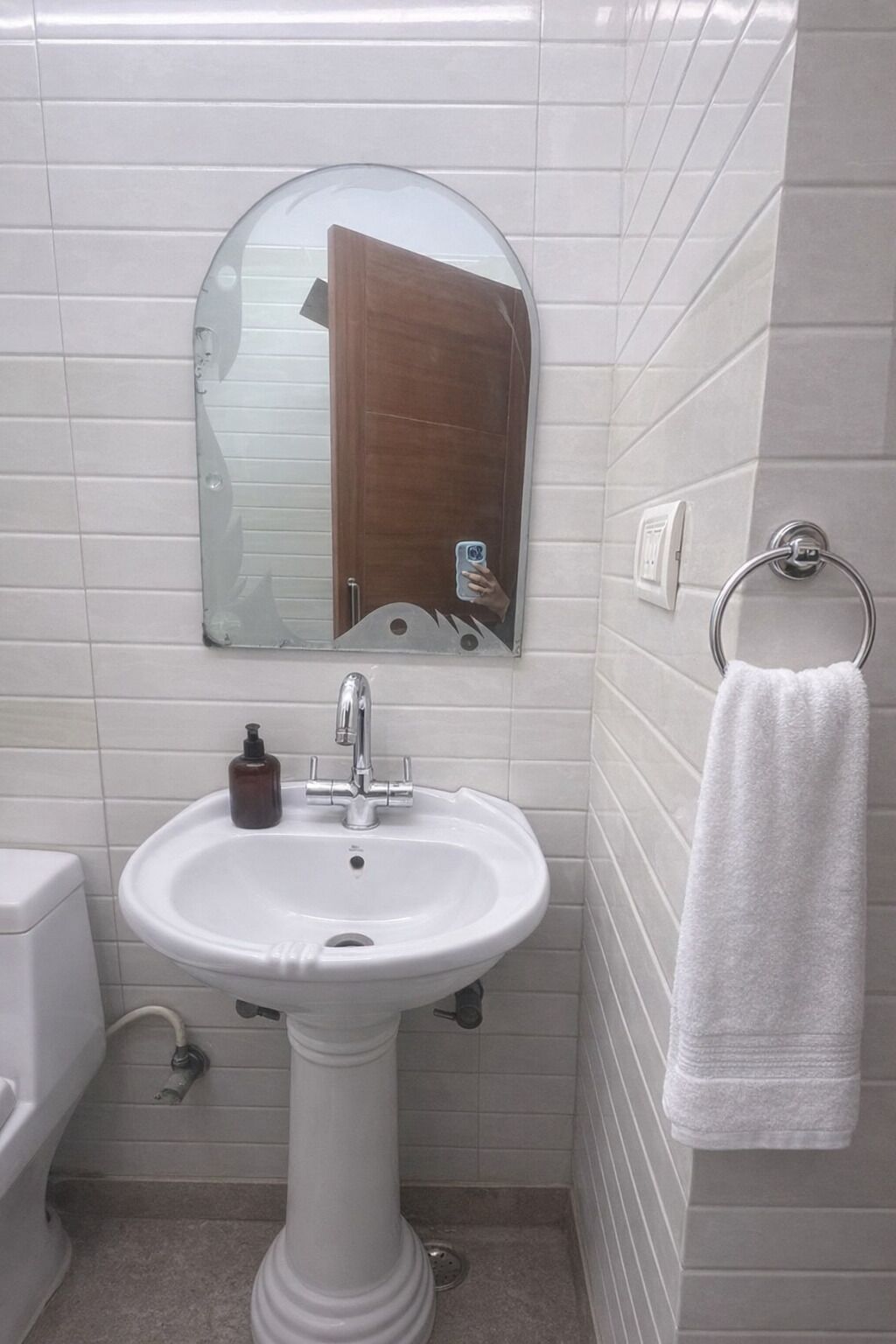A bathroom with a white pedestal sink, a mirror, a towel rack, and a toilet.